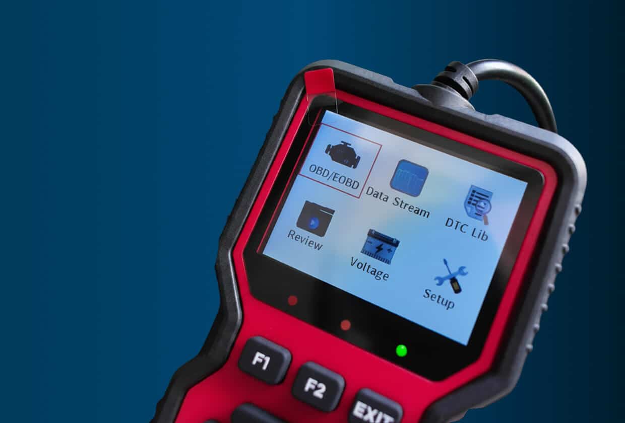 Vehicle testing and diagnostics in Madison, WI at Torque Automotive. A close-up of a handheld automotive diagnostic scanner with a color screen displaying menu options such as OBD/EOBD, Data Stream, DTC Lib, Review, Voltage, and Setup against a blue background.
