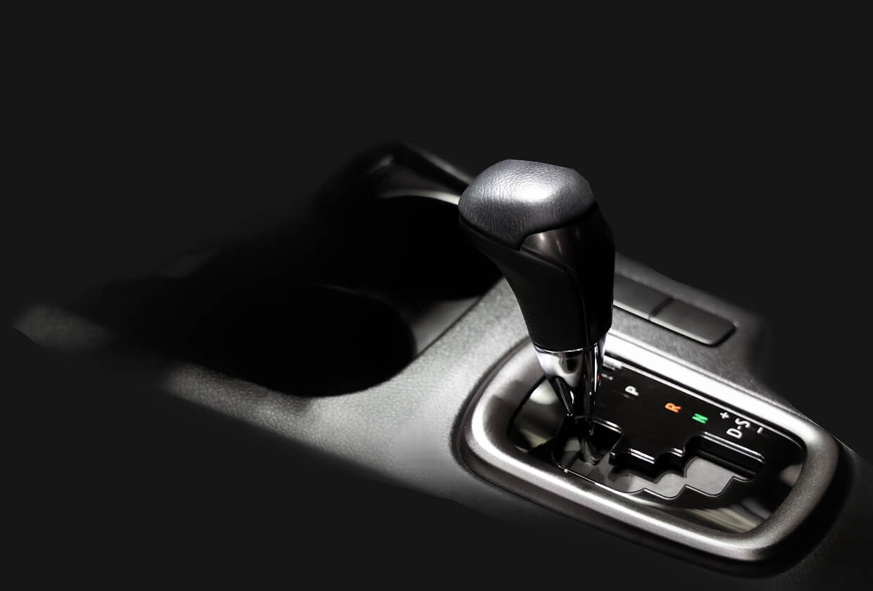 Transmission repair and replacement in Madison, WI at Torque Automotive. Close-up of a black automatic car gear shift lever and part of the console, with cup holders visible in a dimly lit interior against a dark background.