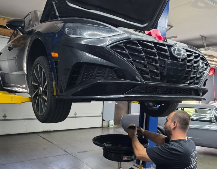 Asian vehicle repair in Madison, WI at Torque Automotive. A mechanic changes the oil on a black Hyundai sedan lifted in an auto repair shop, with the cars hood open and tools visible.